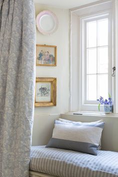 a bed sitting under a window next to a white wall with pictures on it's side