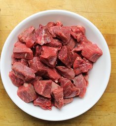 a white bowl filled with raw meat on top of a wooden table next to a knife and fork