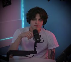 a man sitting in front of a microphone with headphones around his neck and wearing a white t - shirt