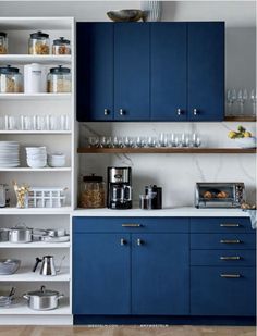 a kitchen with blue cupboards and white counter tops is pictured in this image, there are many dishes on the shelves