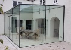 a glass walled dining room in front of a white house with an outdoor table and chairs