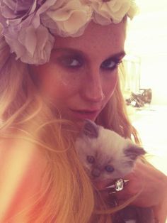 a woman holding a small kitten in her arms and wearing a flower headband on top of her head