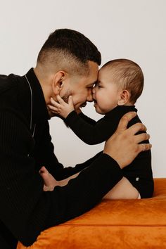 a man holding a small child in his lap and kissing it's face with both hands