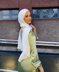 a woman in a hijab is walking down the street with her hand on her hip