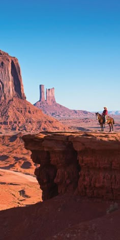 two people riding horses on the edge of a cliff in monument national park, utah