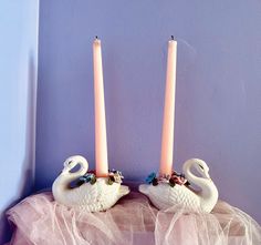 two candles with swans on them sitting next to each other in front of a purple wall