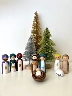 small wooden nativity figurines in front of christmas trees