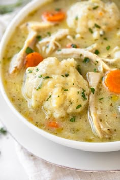 a bowl of chicken and dumpling soup on a white plate with a napkin next to it