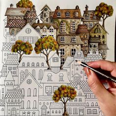 a person is holding a pencil and drawing houses on paper with trees in the foreground