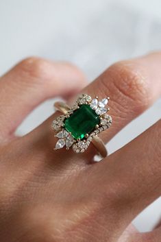 a woman's hand with an emerald and diamond ring on her finger, showing the center stone