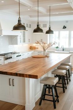 a large kitchen island with stools in front of it and lights hanging from the ceiling