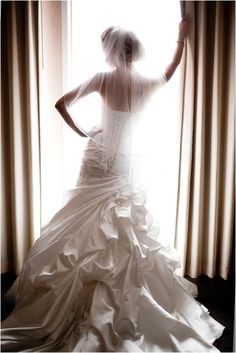 a woman in a wedding dress looking out the window