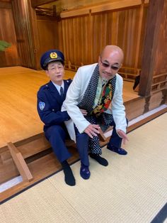 two men in suits and ties sit on the floor next to each other, both wearing sunglasses