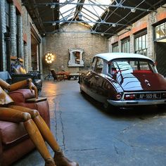 an old fashioned car is parked in a building with exposed ceilings and leather couches