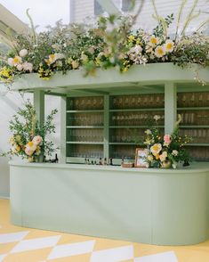 an outdoor bar with flowers and greenery on the top shelf in front of it