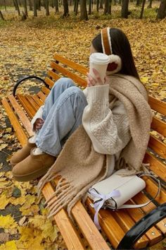 a woman sitting on top of a wooden bench next to a pile of autumn leaves