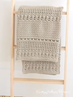 a crocheted blanket is hanging on a ladder next to a white wall and wooden frame