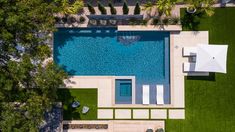 an aerial view of a swimming pool surrounded by lush green grass and white umbrellas