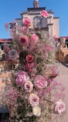 a vase filled with lots of pink and white flowers on top of a table next to a building