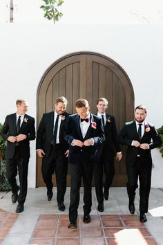 a group of men standing next to each other in front of a wooden door wearing tuxedos