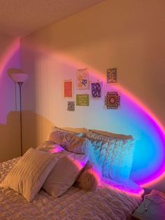 a bed with white sheets and pillows under a rainbow colored light