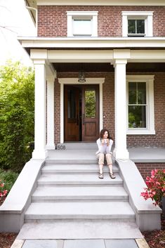 a woman sitting on steps in front of a brick house with white pillars and columns