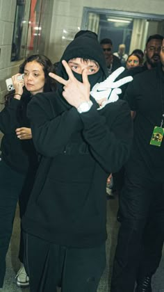 a man in a black hoodie making the peace sign with his hands while others look on