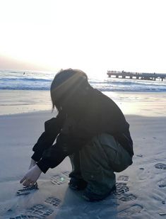 a woman kneeling down on top of a sandy beach