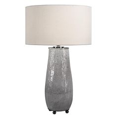 a table lamp with a white shade on it and a black casteor wheel underneath