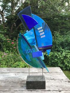 a blue sculpture sitting on top of a wooden table in front of some bushes and trees