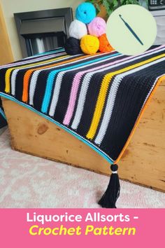 a crocheted blanket on top of a wooden box with balls of yarn in the background