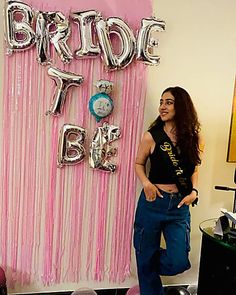 a woman standing in front of a pink backdrop with the word bride to be on it