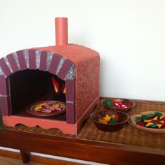 a small brick oven sitting on top of a wooden table next to bowls and plates