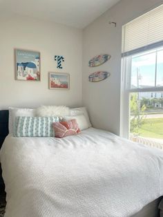 a white bed sitting in a bedroom next to a window with two surfboards hanging on the wall