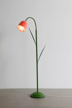 a green floor lamp with an orange shade on it's base and a white wall in the background