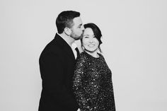 a man and woman standing next to each other in front of a white wall wearing black