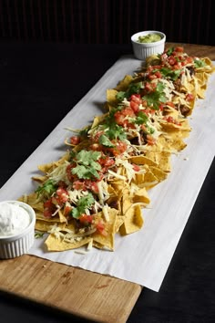 nachos with salsa and sour cream on a wooden platter