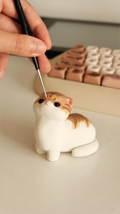 a hand is holding a pen over a cat figurine