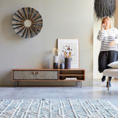 a woman standing in a living room next to a white chair and table with a rug on it