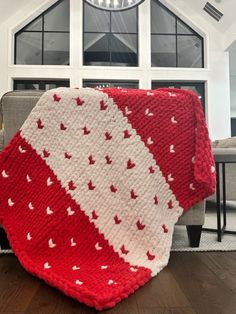 a red and white crocheted blanket sitting on top of a wooden floor next to a couch