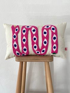 a pink and blue decorative pillow sitting on top of a wooden stool