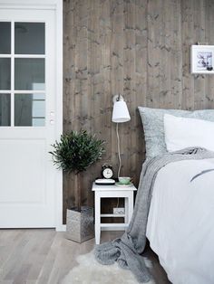 a white bed sitting next to a wooden wall with a plant on top of it