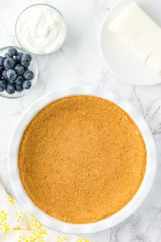 blueberries and cheese are in bowls next to a pie crust on a marble countertop