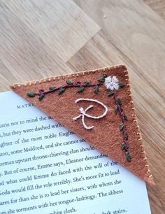 a piece of felt with embroidered letters and flowers on it laying on top of an open book