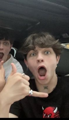 two young men sitting in the back of a car with their hands up and pointing at something