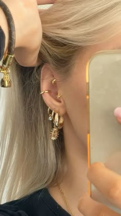 a woman with blonde hair is looking at her cell phone and wearing gold ear rings