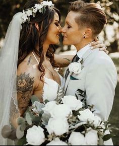 a bride and groom kissing each other in front of some trees with white flowers on their wedding day