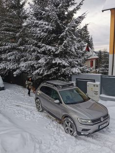 a car is parked in the snow next to some pine trees and a man walking by