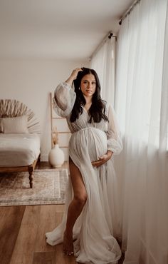 a pregnant woman poses for a photo in her white gown with sheer sleeves and thigh high slits