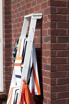 a ladder leaning against a brick wall with towels hanging from it's sides and an orange bag next to it